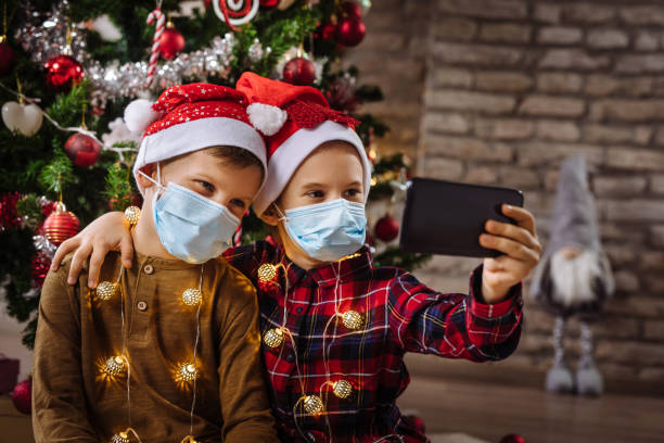istock Two siblings with protective face masks on taking Selfie in front of the Christmas tree 1281790261