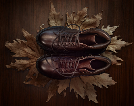 Pair of brown male hiking boots on fallen autumn leaves, top view