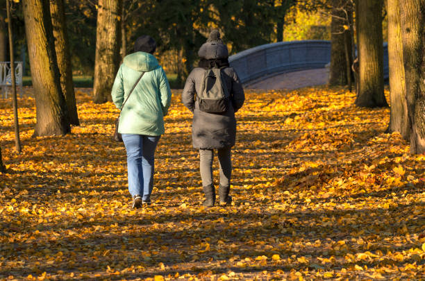 Indian autumn two unidentified women walk through a picturesque sunny park view of their backs