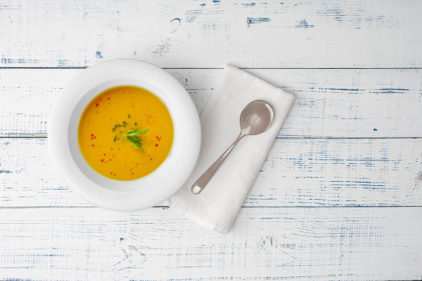 istock Pumpkin soup in a white ceramic plate on a wooden table. Top view. 1281797329