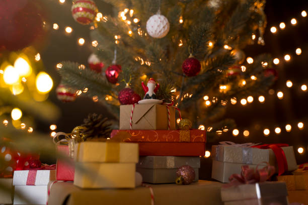 istock Santa claus doll and stack of gift boxes under decorated christmas tree and bokeh lights background 1281798624