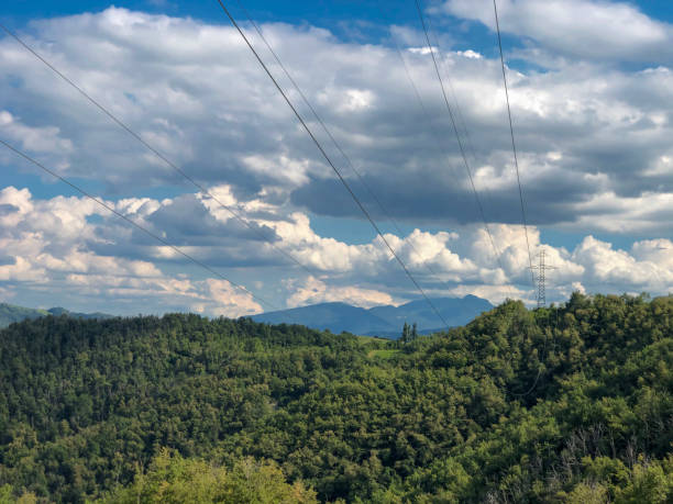 istock Electricity infrastructure. power lines across mountains landscape, blue sky, green fields and path. Energy industry. Copy space 1281799710