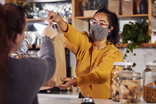 Service that's friendly and hygienic Shot of a woman wearing a mask while serving a customer in a cafe cafe culture photos stock pictures, royalty-free photos & images