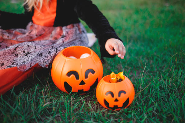 a child's hand reaches for candy in a pumpkin-shaped candy basket