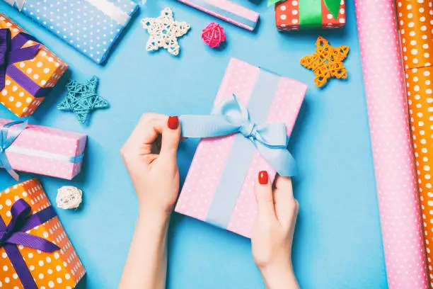 Photo of Top view of female hands holding a Christmas present on festive blue background. Holiday decorations and wrapping paper. New Year holiday concept