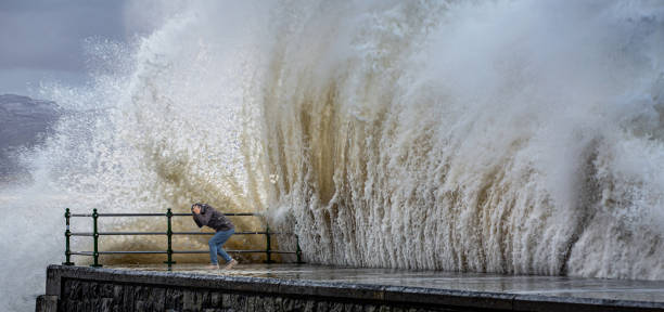 istock Huge wave breaks on to a quayside with a spectator taking cover from the spray 1281808758