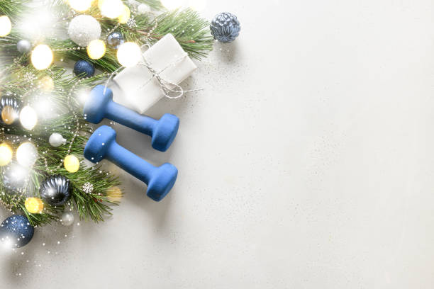 composición de fitness de navidad con mancuernas azules, regalo sobre fondo blanco con bokeh y espectáculo. - holiday healthy lifestyle weight christmas fotografías e imágenes de stock