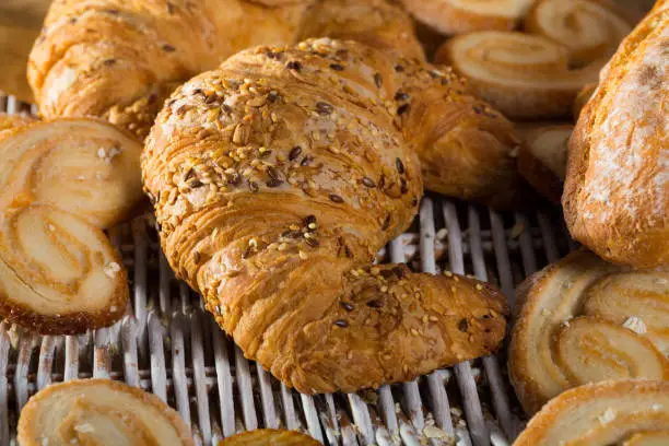 Closeup of fresh croissant sprinkled of sesame and linseeds on rattan mat with other bakery goods