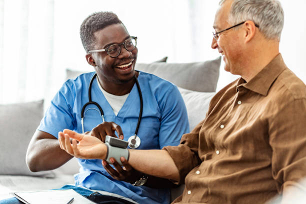 Caretaker measuring mature man's blood pressure African-American Male Nurse Measuring Blood Pressure of Mature Patient in the Livingroom. home caregiver stock pictures, royalty-free photos & images