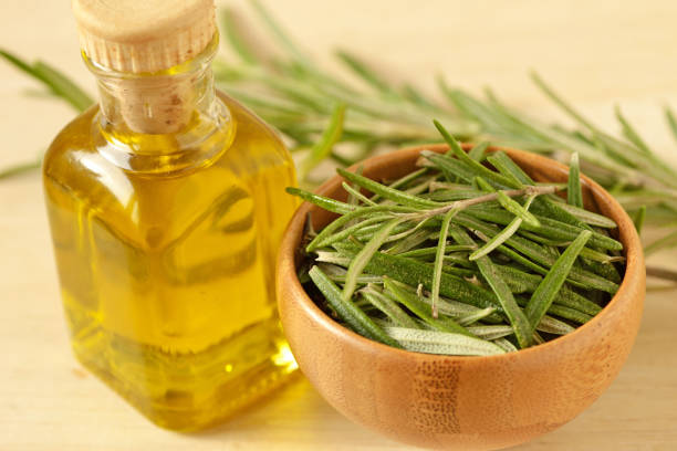 Small bottle of rosemary infused oil and fresh rosemary leaves in wooden bowl stock photo