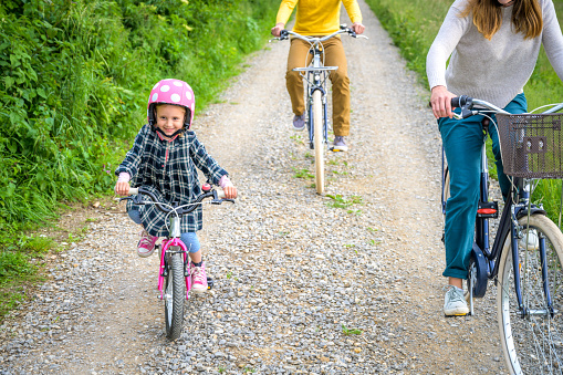 Family together. Little girl with parents on bike trip. Smiling Caucasian girl riding her bicycle. Active relaxation in nature concept.