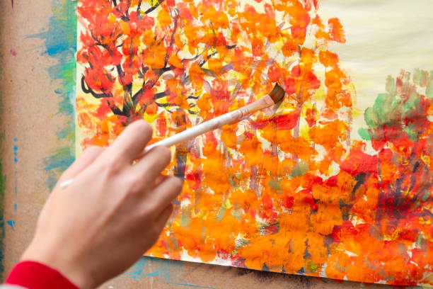 Young artist paints orange autumn trees on canvas