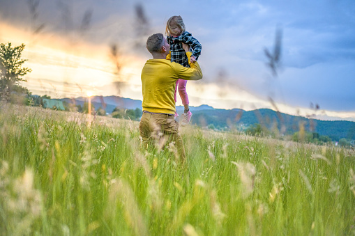 Young daddy enjoying time with daughter. Man lifting little girl. Sunset time. Family together concept.