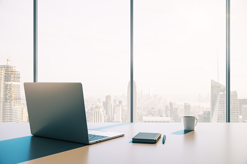 Laptop with a cup of coffee on the desktop against the background of a window with a city view. 3D Rendering