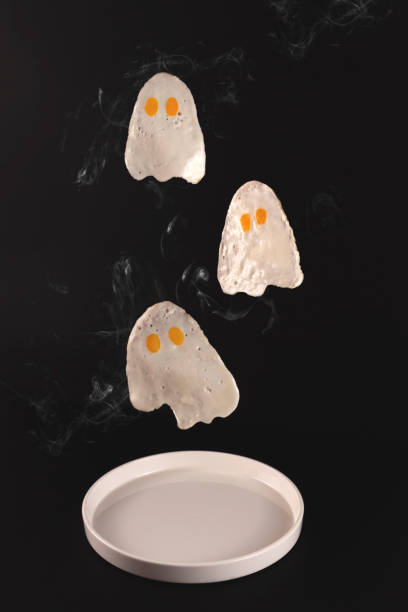 istock Fried eggs in the form of ghosts fly over a white plate on a black background 1281838218