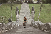 Beautiful Girl Climbing Up Stone Stairs In Pura Lempuyang Temple In Bali, Indonesia. Young Woman Explores Ancient Architecture In Karangasem.