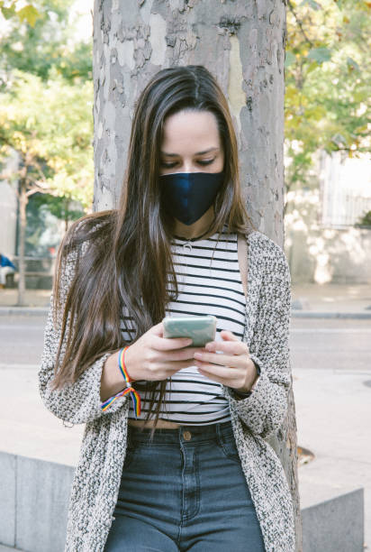 istock Woman in mask using smartphone on street 1281841183