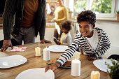 Happy African American boy setting the table for family lunch during holidays.