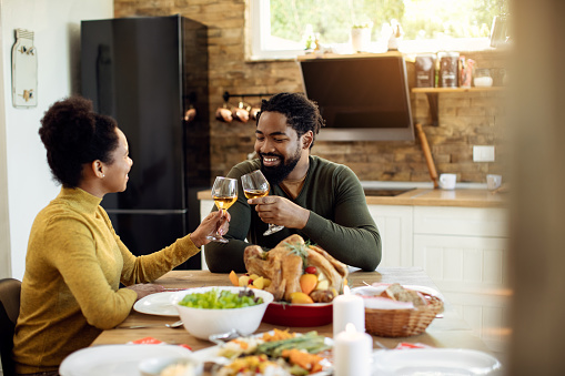 Happy black couple tasting with wine while having Thanksgiving lunch at dining table.