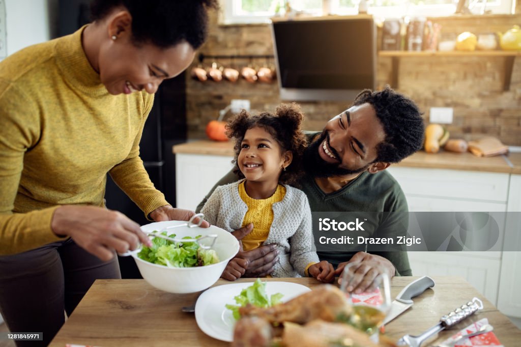 Feliz chica afroamericana almorzando el Día de Acción de Gracias con sus padres en la mesa de comedor. - Foto de stock de Familia libre de derechos