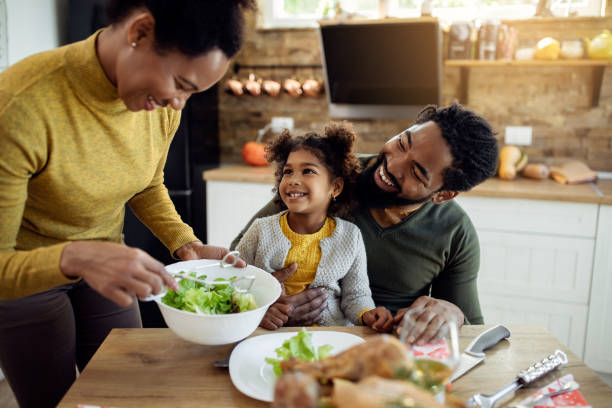 Happy African American girl having Thanksgiving lunch with her parents at dining table. Happy black family celebrating Thanksgiving and having lunch together in dining room. Focus is on girl. dining photos stock pictures, royalty-free photos & images
