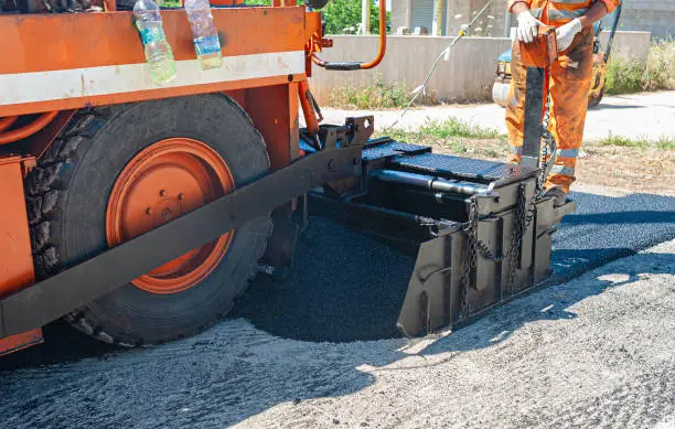 Photo of New Road - Pavement machine laying fresh asphalt or bitumen on top of the gravel base during highway construction