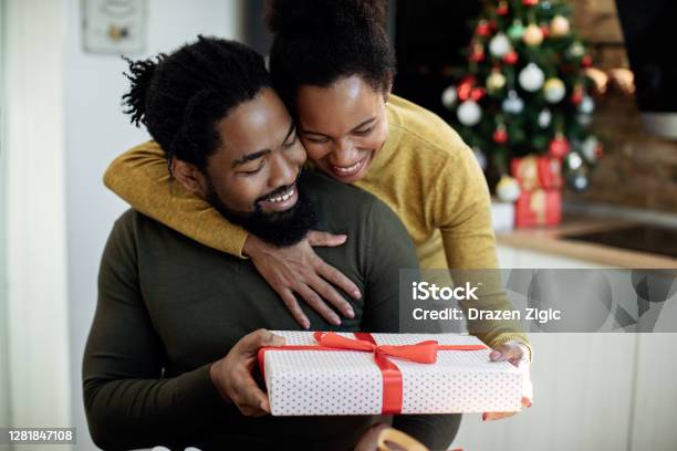 Happy African American Woman Surprising Her Husband With Christmas Present Stock Photo - Download Image Now