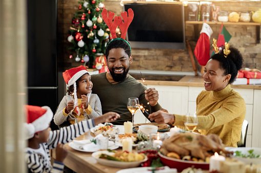 istock Feliz familia negra divirtiéndose con chispas durante el almuerzo de Navidad en el comedor. 1281847249