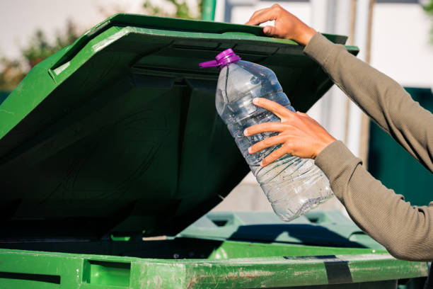 istock Man throwing out empty non-recyclable plastic aqua bottle in to green garbage container 1281852666