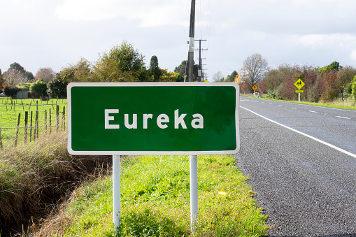 Eureka town welcome road sign on left side of a road on a village background. New Zealand, North Island