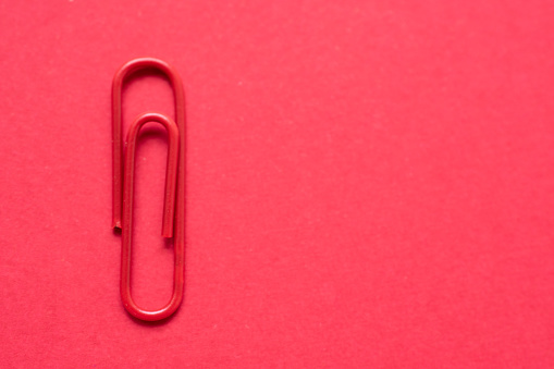 Red paper clip over a cherry red background, with copy space at the right side of the photo