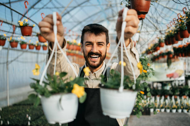 Happy middle age worker or owner working in greenhouse with beautiful potted flowers and house plants. Small business concept.