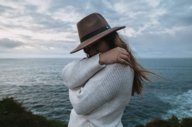 Young woman by the sea hugging self