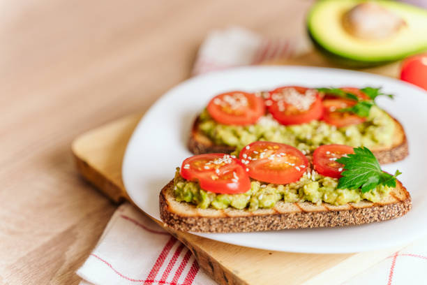 istock toasted bread with avocado paste and fresh tomato. Avocado mixed with lemon juice is spread on bread.  health food concept, vegan, vegetarian 1281860592