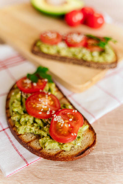 istock toasted bread with avocado paste and fresh tomato. Avocado mixed with lemon juice is spread on bread.  health food concept, vegan, vegetarian 1281860599
