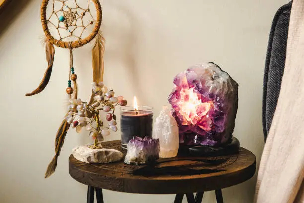 Photo of Relaxing home shrine with relaxing objects, amethyst cluster geode lamp illuminated, scented candle burning, selenite tower stone, crystal wire tree and dream catcher.