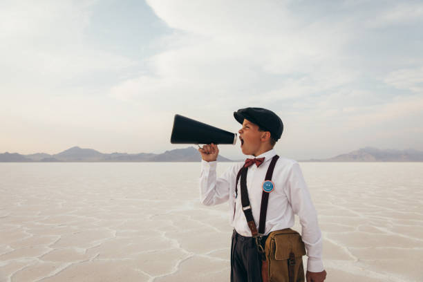 Young Newspaper Boy during COVID A young newspaper boy and teenager stands on the remote salt flats in Utah during the coronavirus pandemic trying to deliver his message. He is wearing old fashioned clothing with a face mask and a megaphone. gossip photos stock pictures, royalty-free photos & images