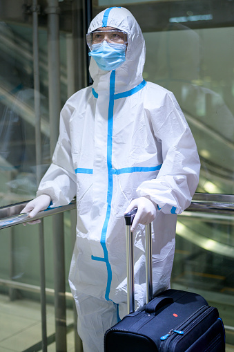 An Asian man is wearing ppe suit in airport elevator , Safety travel , covid-19 protection , social distancing concept .
