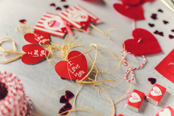 Selective focus of paper heart with 'I love you' message left on a table with different decorative elements around for Valentine's Day.