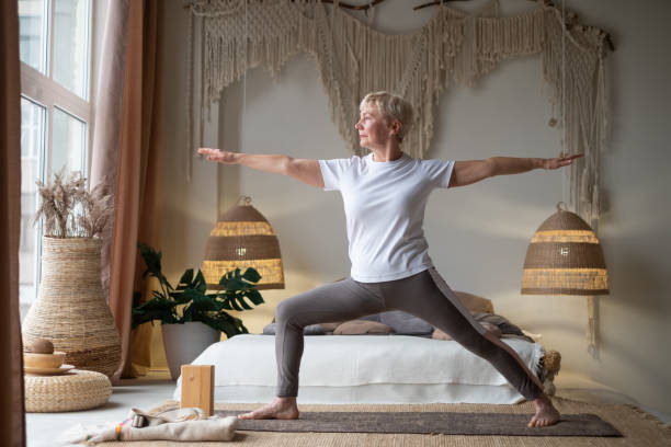 Senior woman practicing yoga, standing in Warrior two exercise, Virabhadrasana II pose Senior woman practicing yoga, standing in Warrior two exercise, Virabhadrasana II pose, working out at home warrior position stock pictures, royalty-free photos & images