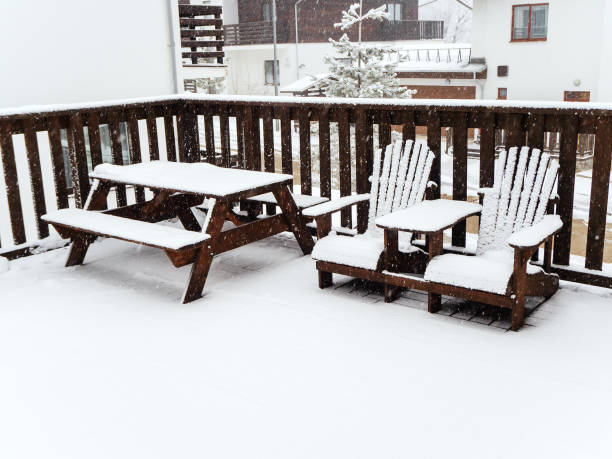 istock Two wooden chairs and a table with benches stand on a snow-covered veranda under a snowfall 1281873462