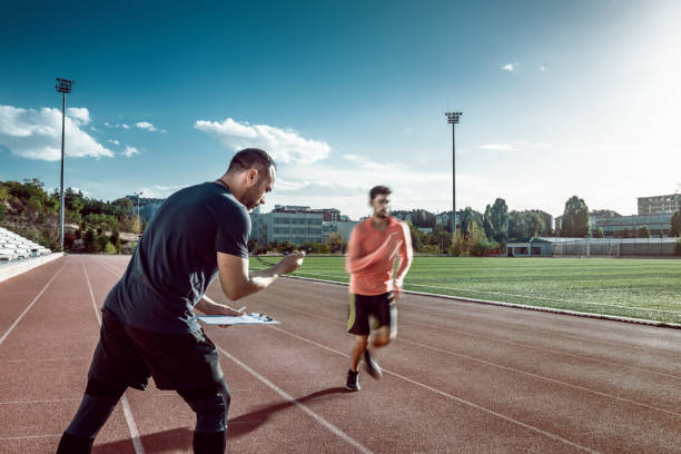 Runner and coach doing sports training on track and field. The coach is measuring results with a stopwatch stock photo