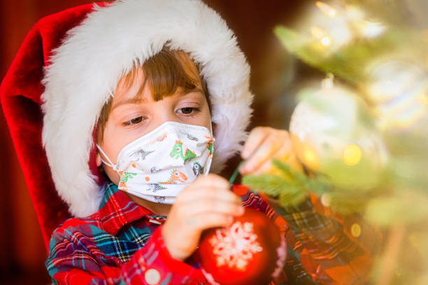 istock Serious Serious pensive Little boy wearing a Santa hat and a protective face mask decorating a Christmas Tree 1281874827