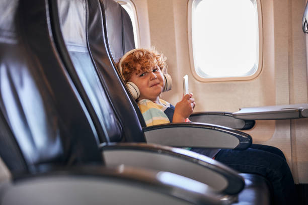 garotinho sentado sozinho com fones de ouvido e tablet em um avião - sadness child little boys loneliness - fotografias e filmes do acervo