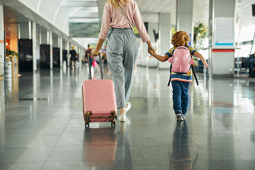 Cropped photo of a female parent rolling her carry-on behind her and walking by the hand with her son