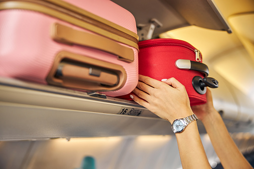 Arms shoving a small piece of luggage to the top shelf of an aircraft
