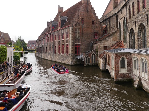 Belgium, Bruges, May 10 2019 234 pm, the left bank of the canal is a drop-off station for sightseeing boats, on the right bank historical buildings in red brick construction, with a church background