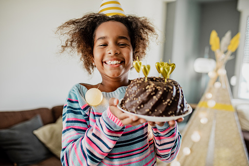 African American girl holding a birthday cake and she is looking at camera