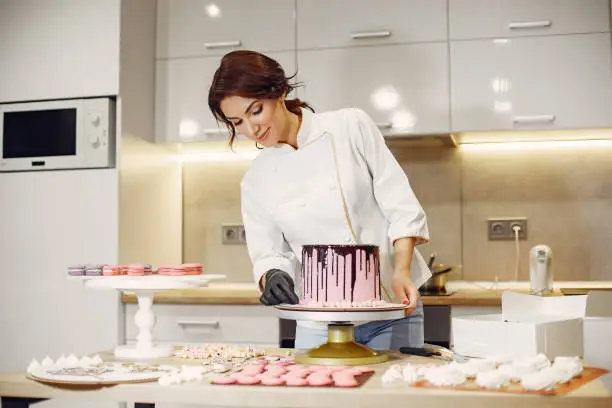 Confectioner in a kitchen. Woman in a uniform. Professional decorates the cake.