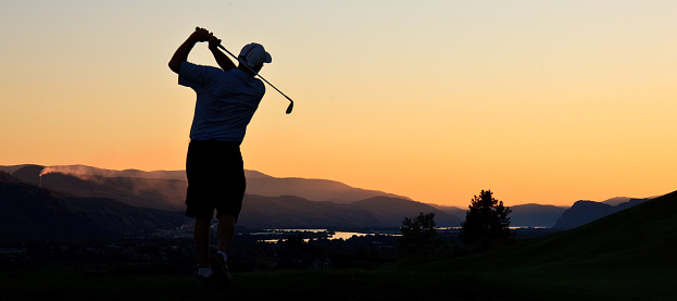 A golfer at sunset. Male golfer. Unrecognizable. Back view. Golfer is in classic finish position pose.